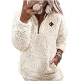 A person wears a cream-colored, plush, sherpa pullover with a quarter-zip front and a small emblem. The outfit includes a matching phone case, watch, and bracelets.