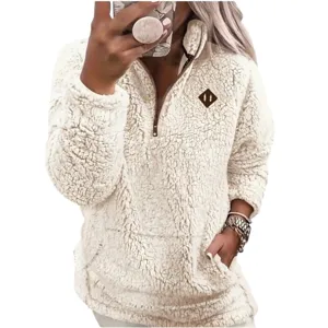 A person wears a cream-colored, plush, sherpa pullover with a quarter-zip front and a small emblem. The outfit includes a matching phone case, watch, and bracelets.