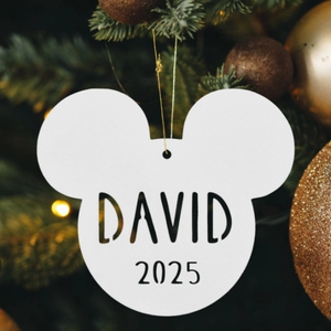 A Mickey Mouse-shaped ornament with the name \“David\“ and the year \“2025\“ hangs on a Christmas tree amid gold and bronze baubles.