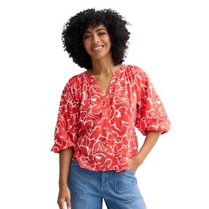 A woman is wearing a red and white floral-patterned blouse with elbow-length puffy sleeves and a V-neck, paired with blue jeans.