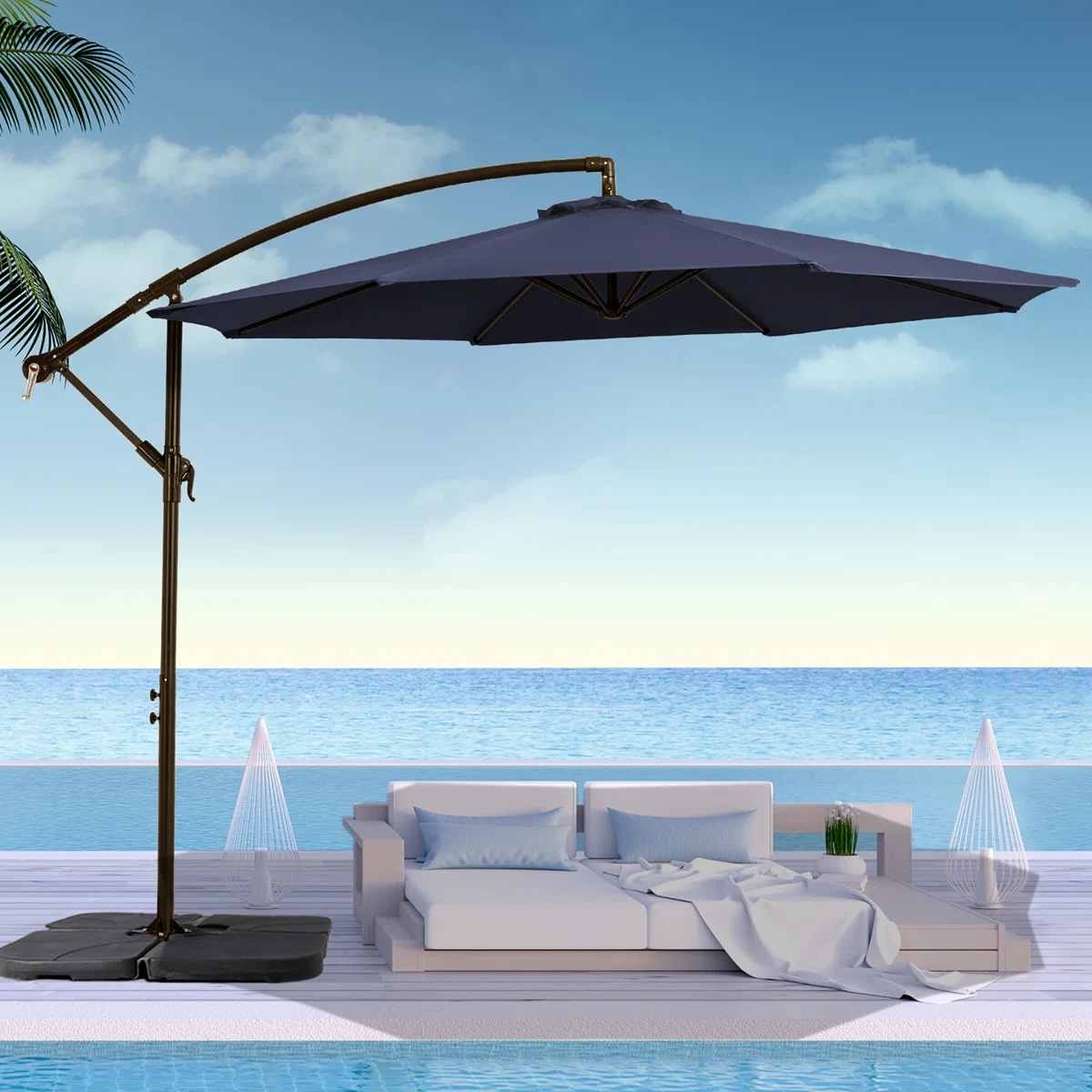A blue cantilever patio umbrella provides shade over a modern outdoor sofa set by the pool, with a background of ocean and sky.