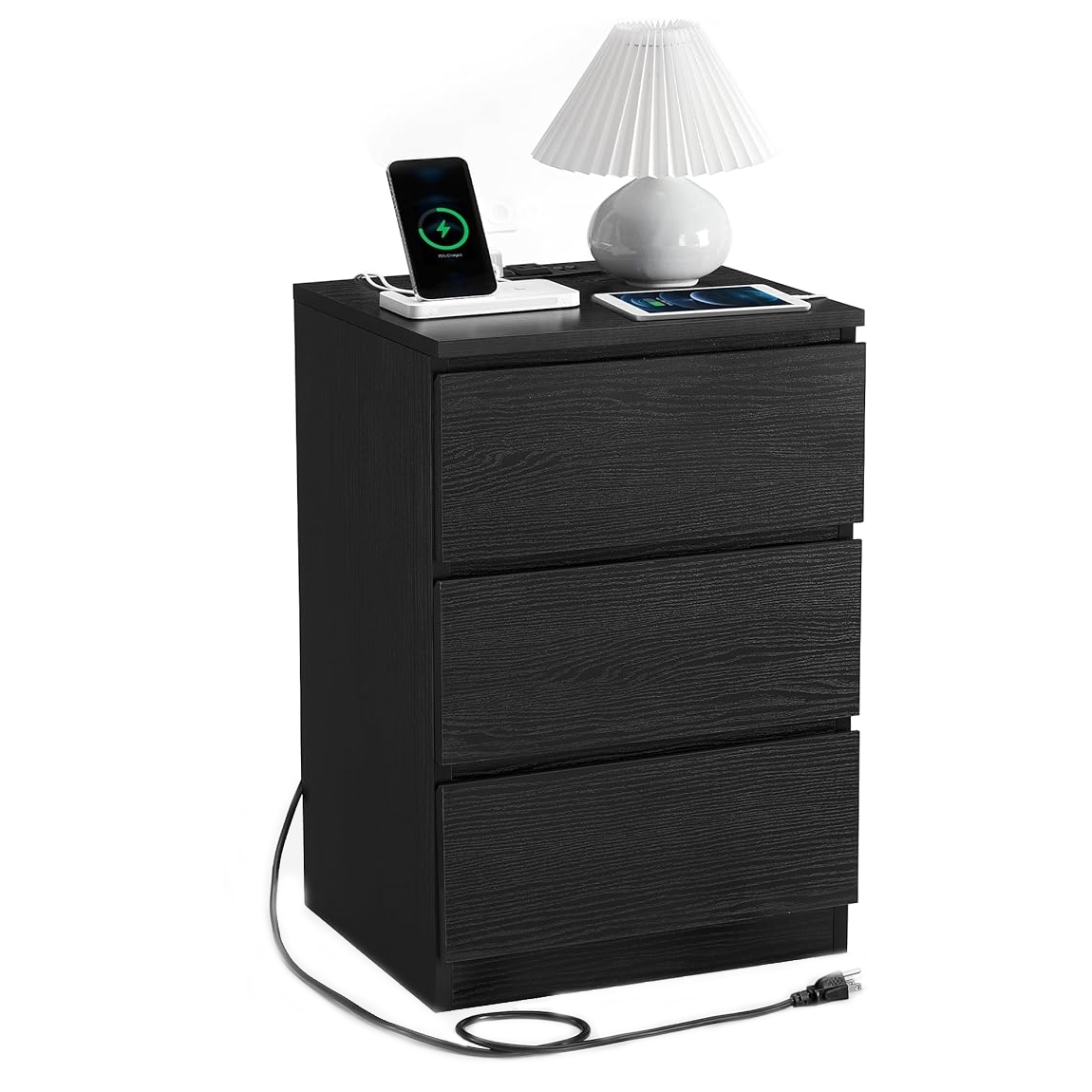 A black three-drawer nightstand features a built-in wireless charging station, depicted with a phone and tablet charging on top. A white lamp sits beside them, with a power cord extending from the back.