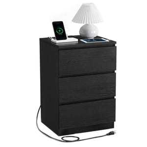 A black three-drawer nightstand features a built-in wireless charging station, depicted with a phone and tablet charging on top. A white lamp sits beside them, with a power cord extending from the back.