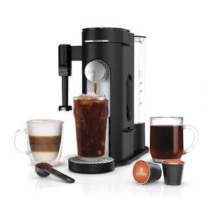 A Ninja Specialty Coffee Maker brews various coffee types, including iced coffee, and features a spout for direct dispensing. It comes with a glass of iced coffee, a cup of layered coffee, and a cup of hot coffee, alongside coffee pods and a scoop.