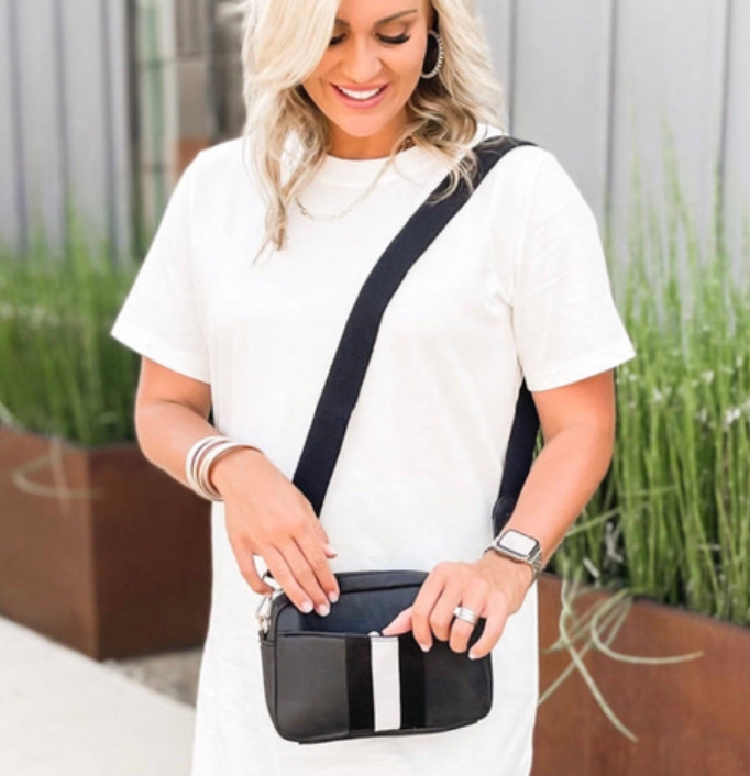A woman is wearing a white T-shirt, accessorized with a black crossbody bag, silver bracelets, a watch, and rings.
