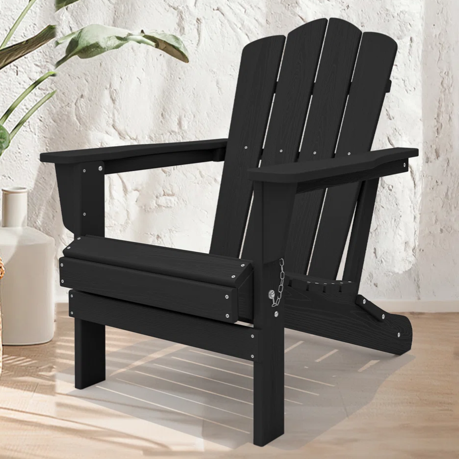 A black Adirondack chair is placed on a light wood floor next to potted plants and a white vase, set against a textured white wall.
