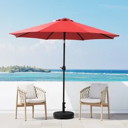 A red patio umbrella with a black base stands between two wicker chairs with white cushions, set on a terrace overlooking the ocean.