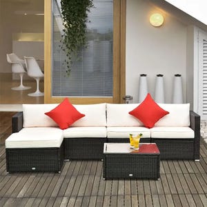 Outdoor wicker sectional sofa with white cushions and red pillows, accompanied by a matching wicker coffee table on a wooden deck.