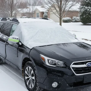A black Subaru with a windshield cover protecting against snow in a residential area during winter.