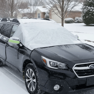 A black Subaru with a windshield cover protecting against snow in a residential area during winter.