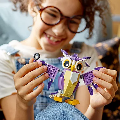 A child is holding a purple and white LEGO owl with posable wings and large eyes; the set allows for the creation of different forest creatures.