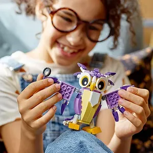 A child is holding a purple and white LEGO owl with posable wings and large eyes; the set allows for the creation of different forest creatures.