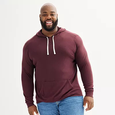 A man wears a maroon double-knit hoodie with long sleeves, a drawstring hood, and a front pouch pocket, paired with blue jeans.