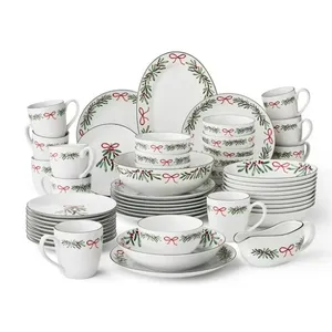 Set of holiday-themed dinnerware with red and green adornments, including plates, bowls, mugs, and serving pieces, featuring ribbon and evergreen designs.