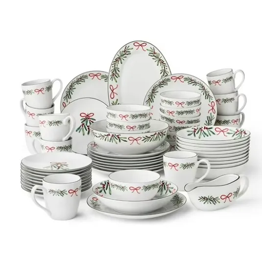 Set of holiday-themed dinnerware with red and green adornments, including plates, bowls, mugs, and serving pieces, featuring ribbon and evergreen designs.