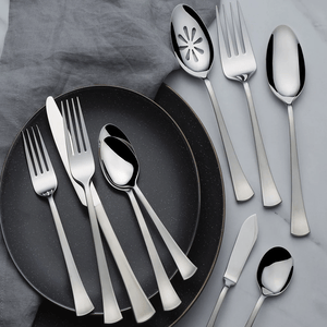 A set of stainless steel flatware includes forks, knives, and spoons arranged on two dark plates and a gray cloth.