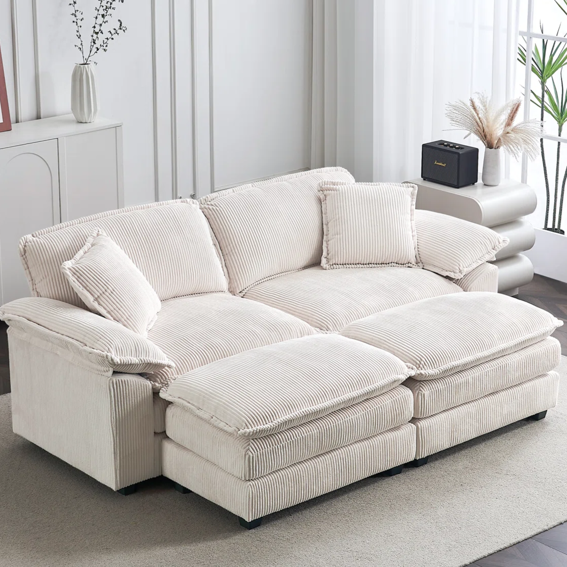 A beige corduroy sectional sofa with cushioned seats and backs, placed in a light-filled living room with decorative plants and accessories.