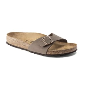 A taupe-colored Birkenstock sandal featuring a single wide strap with an adjustable metal buckle and a textured cork footbed for comfort.