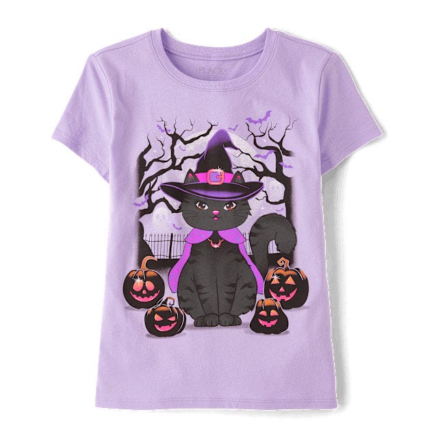 A lilac T-shirt featuring a black cat wearing a witch's hat and purple scarf, surrounded by pumpkin lanterns in a spooky Halloween scene with bare trees in the background.