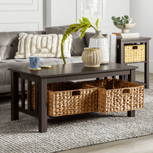 A dark wood coffee table with slatted sides features two woven storage baskets in the lower shelf, a textured rug underneath, and decorative items like vases and a mug on top.