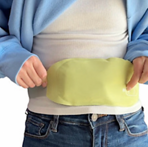 A person places a yellow-green portable heating pad on their lower abdomen. The pad is designed for pain relief and warmth, and its size and flexibility make it suitable for covering a range of body parts.