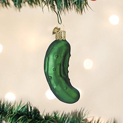 A green pickle-shaped Christmas ornament hangs on a tree branch, featuring a gold cap and a hook for hanging.