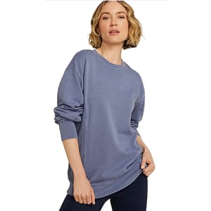 A woman wearing a loose-fitting, long-sleeved blue sweatshirt with ribbed cuffs and a waffle pattern detail on the sides, paired with dark leggings.