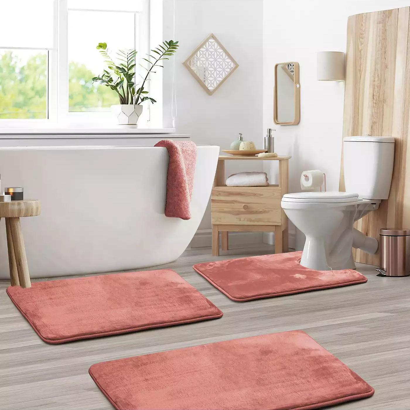 Three coral bathroom mats placed in front of a bathtub, toilet, and sink in a modern bathroom setting.