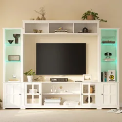 A white entertainment center with shelves and cabinets, holding a flat-screen TV, books, decor items, speakers, and a record player. Soft lighting highlights the shelves.