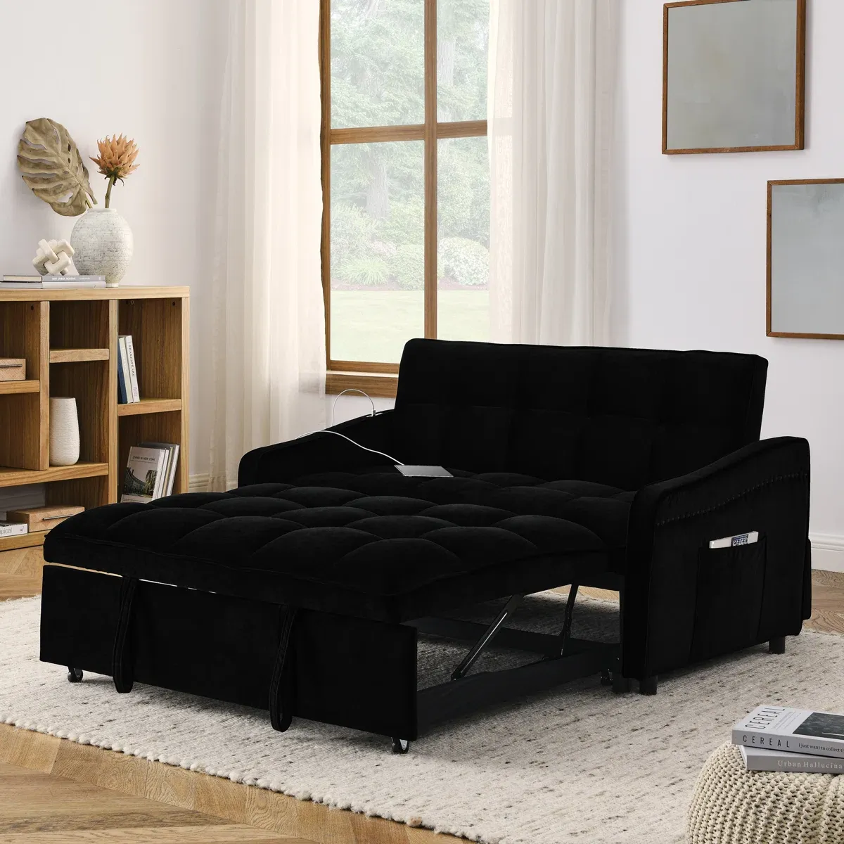 A black tufted sleeper sofa is extended to form a bed, placed in a living room with a light rug, wooden floor, and bookshelves.
