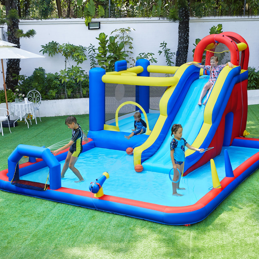 An inflatable water park featuring a slide, splash pool, basketball hoop, and water cannon, with kids playing on a grass lawn.