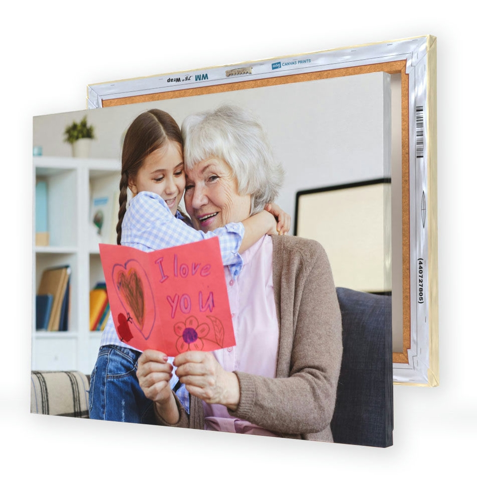 A canvas print displays a joyful scene of a young girl hugging an elderly woman, who is holding a handmade card that says \“I love you,\“ featuring a heart and a flower drawing.
