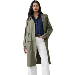 A model wears an olive green parka with a hood, a blue button-up shirt, white wide-leg pants, a brown belt, and black loafers.