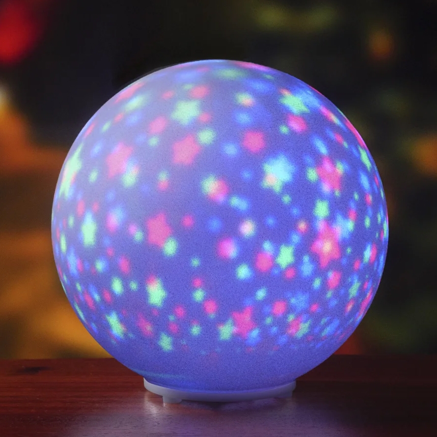A glowing spherical lamp with colorful star and dot projections in blue, pink, and green hues, creating a festive atmosphere.