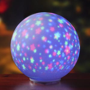 A glowing spherical lamp with colorful star and dot projections in blue, pink, and green hues, creating a festive atmosphere.