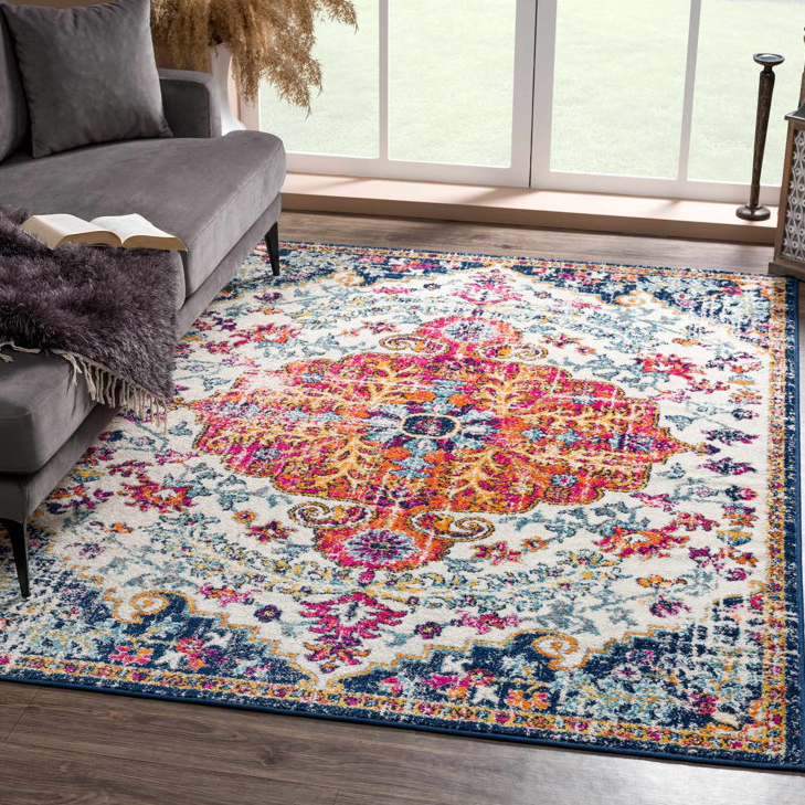 A vibrant boho area rug measuring 5' x 7' features an intricate pattern with a bold central medallion, showcasing a mix of pink, orange, blue, and gold colors on a cream background, adding a lively touch to the living room setting.
