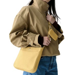A person is wearing a tan jacket and holding a yellow handbag with a matching smaller pouch attached.