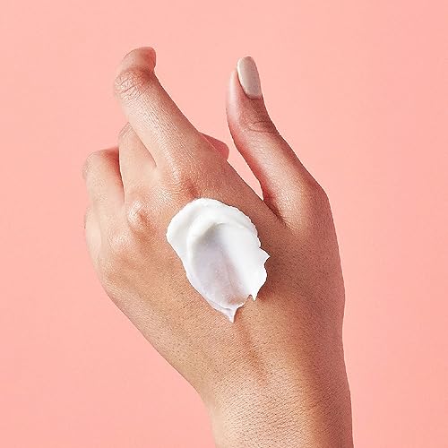 A hand with a dab of white cream on it against a pink background.