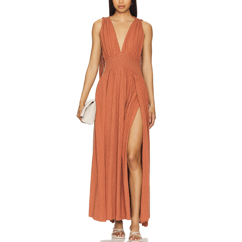 Rust-colored convertible halter maxi dress featuring a deep V-neckline, high front slit, and sleeveless design, paired with a white clutch and strappy white heels.