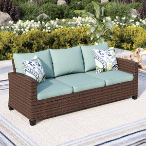 Outdoor wicker sofa with teal cushions and patterned throw pillows, set in a garden. A dog is visible to the side.