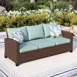 Outdoor wicker sofa with teal cushions and patterned throw pillows, set in a garden. A dog is visible to the side.