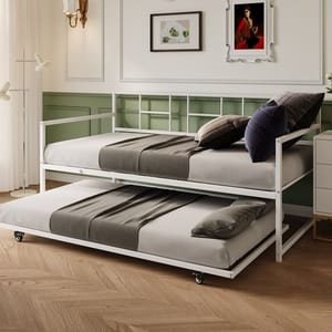 A white metal daybed with a pull-out trundle bed is shown, both featuring grey bedding and pillows. The room is decorated in a classic style with light green paneling, framed artwork, and warm wooden floors.