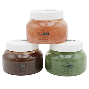 Three jars of \“Lola Soap\“ soft salt glow scrub in shades of orange, brown, and green with white lids.