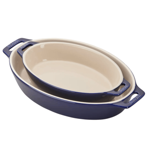 Two oval baking dishes with a blue exterior and cream interior, featuring handles labeled \“STAUB.\“ They are stacked together, with the smaller dish nested inside the larger one.