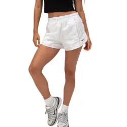 A woman is wearing a black cropped T-shirt with \“NXE\“ lettering, white athletic shorts, Nike socks, and white Nike sneakers.