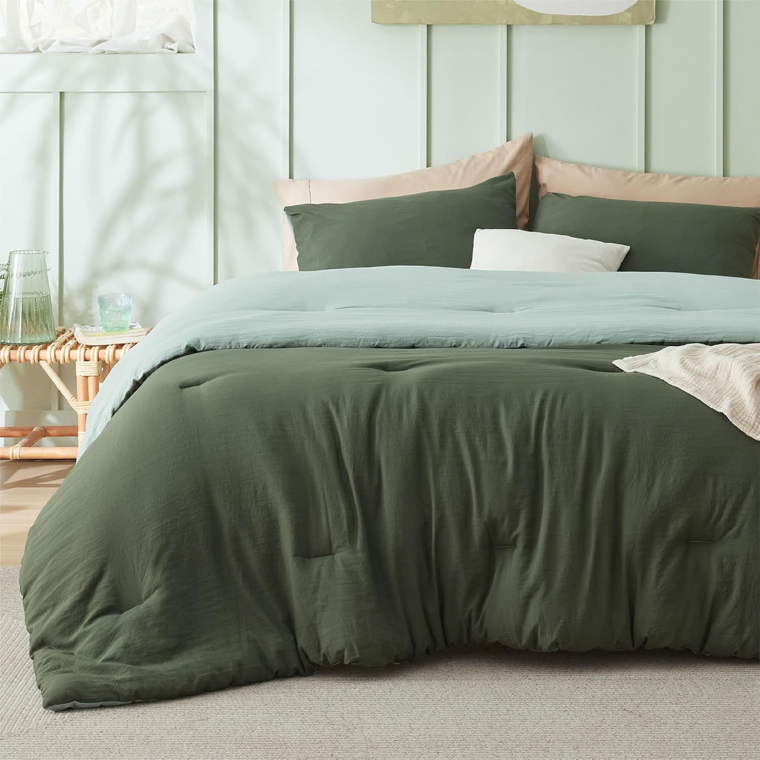 A green three-piece comforter set on a bed, comprising a plush comforter and two pillow shams, in a pastel-hued room with matching decor.