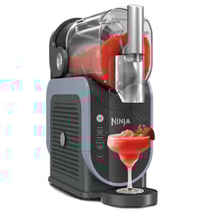 Ninja's new slushie maker features a large horizontal container with a spout for easy dispensing. Controls on the front allow selection of slush, snow, or other beverage options, and the unit serves a strawberry slushie into a glass on its tray.