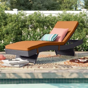 Outdoor chaise lounge with orange cushion, adjustable backrest, and striped pillows on a decorative rug by a pool.