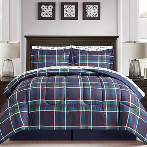 A plaid bedding set, featuring a navy, green, and red pattern, is displayed on a bed with matching pillow shams and white patterned sheets. The room includes a dark wood headboard and symmetrical bedside lamps.