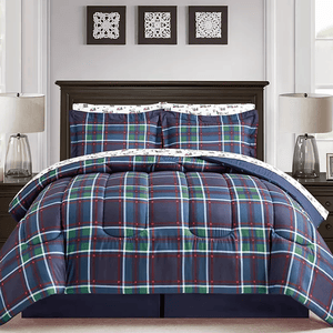 A plaid bedding set, featuring a navy, green, and red pattern, is displayed on a bed with matching pillow shams and white patterned sheets. The room includes a dark wood headboard and symmetrical bedside lamps.
